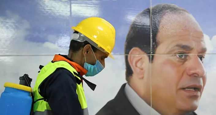 أحد أعضاء الفريق الطبي بجانب لافتة للرئيس المصري عبد الفتاح السيسي أثناء قيامه برش مطهر في محطة مترو الشهداء بالقاهرة كورونا - مصر