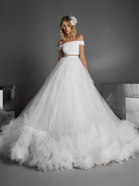 برونوفياس - Pronovias
من برونوفياس، كروب توب بسيطة التصميم، منسدلة الأكتاف، قصيرة عند البطن مع تنورة طويلة ومنفوشة معمولة من طبقات التول الكثيف وقد تزيّنت أطرافها بكشاكش ناعمة عززت من جمال الإطلالة العرائسية هذه وزادتها حيوية.