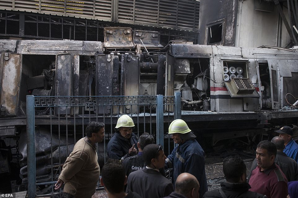 A view of the side of the train shows that it has been completely gutted by flames as fire crews work nearby