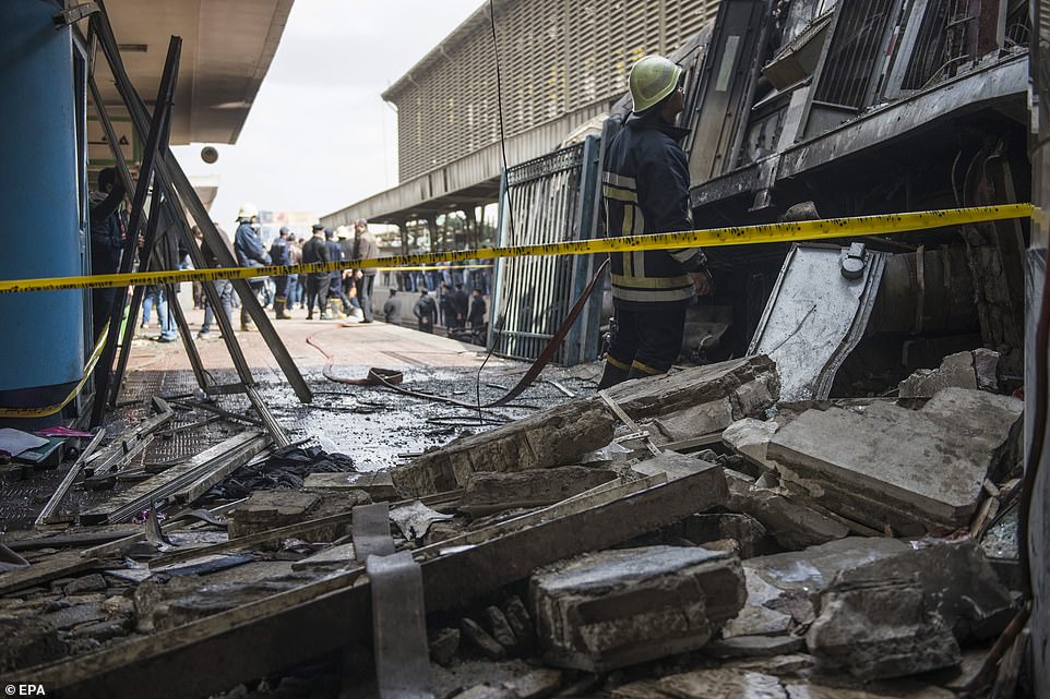 Firefighters stand near damaged train wagons after a fire broke out at the main train station in Cairo