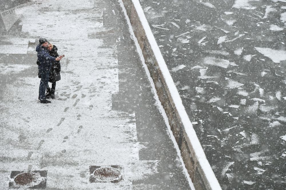 شخصان يلتقطان صورة سيلفي على خلفية تساقط ثلوج كثيف على ضفة نهر موسكو