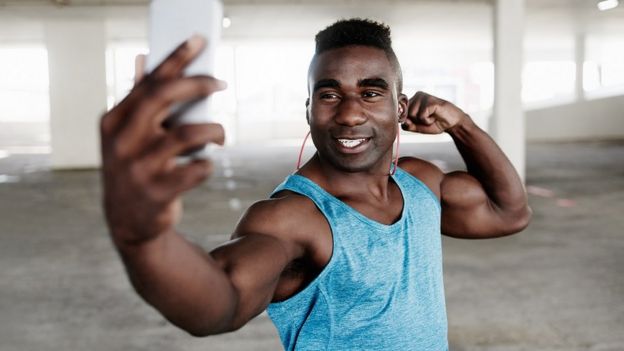 105612918_a7dc3af7-72a7-4e97-8728-bc4af3b6c9e7 لقطة عن قرب لشاب رياضي وهو يلتقط صورة سيلفي بهاتف محمول بينما يمارس تمارين رياضية في موقف سيارات تحت الأرض
