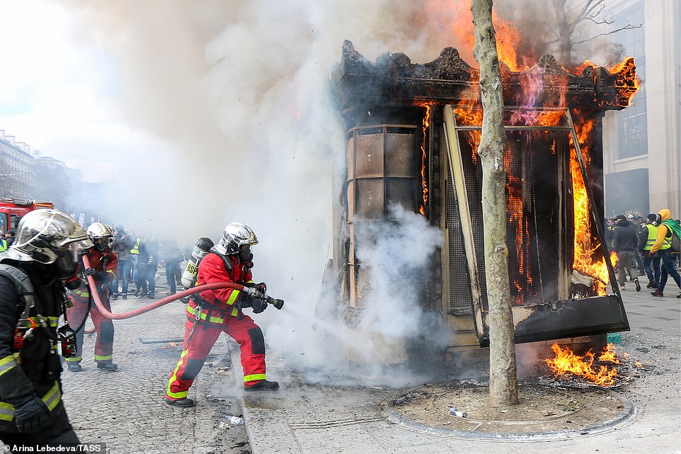 11077790-6816815-image-a-68_1552752006521 Firefighters battle a fire at a street kiosk during a Yellow Vests movement protest as demonstrations continue around them
