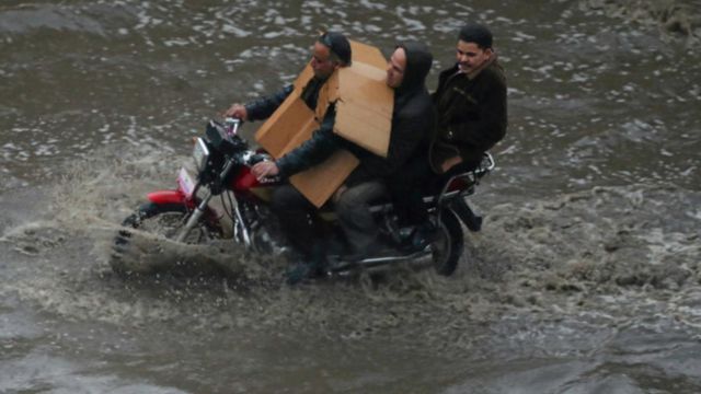 111252037_2 ثلاثة يستقلون دراجة بخارية في شارع تغمره المياه