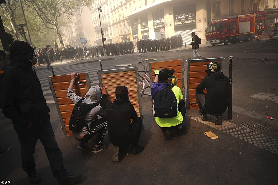 Protestos take shelter behind wooden panels.Â Dozens of black-hooded demonstrators threw rocks at police and some set fire to motor-cycles