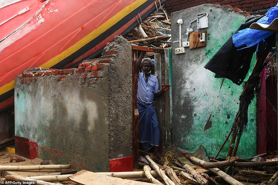13077764-6991719-image-a-8_1556954498615 An Indian man looks out from a damaged building, with a fishing boat lodged on the roof, along the seafront in Puri