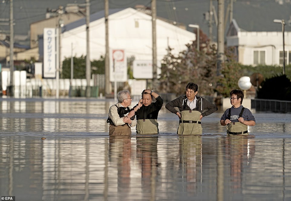 19651642-7567507-image-a-52_1570962258948 Workers standing waist-deep in flood water check the conditions of their office after the passage of Typhoon Hagibis in Nagano
