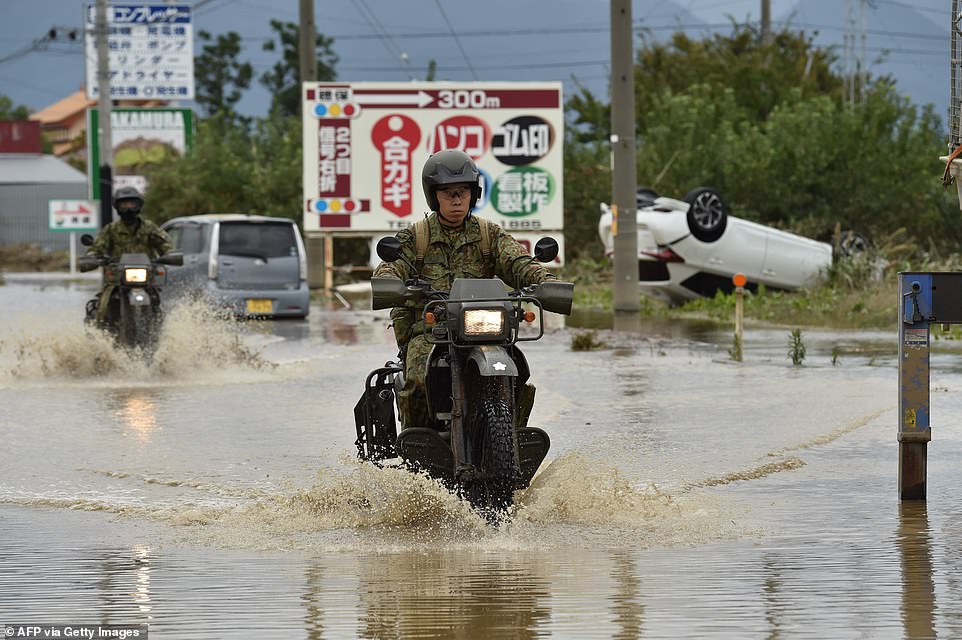 19679930-7570251-image-a-16_1571037614566 Military personnel drove their motorbikes down flooded street in the aftermath of Typhoon Hagibis in Nagano today.Tens of thousands of rescue workers are searching for survivors