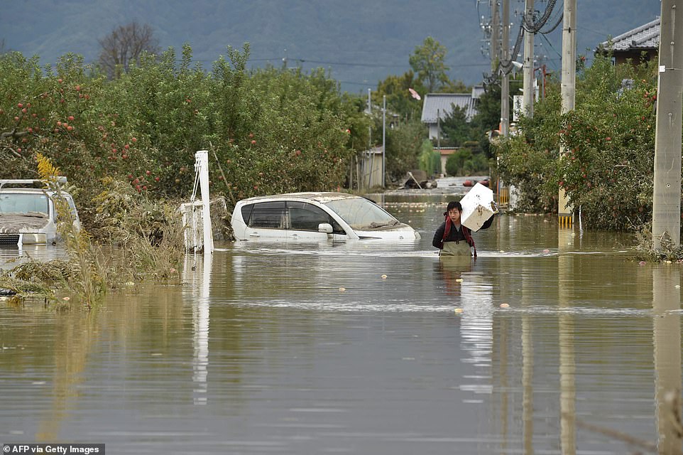 19680310-7570251-image-a-40_1571038560613 A man wading through floodwaters with items salvaged from his house in the aftermath of Typhoon Hagibis, in Nagano today