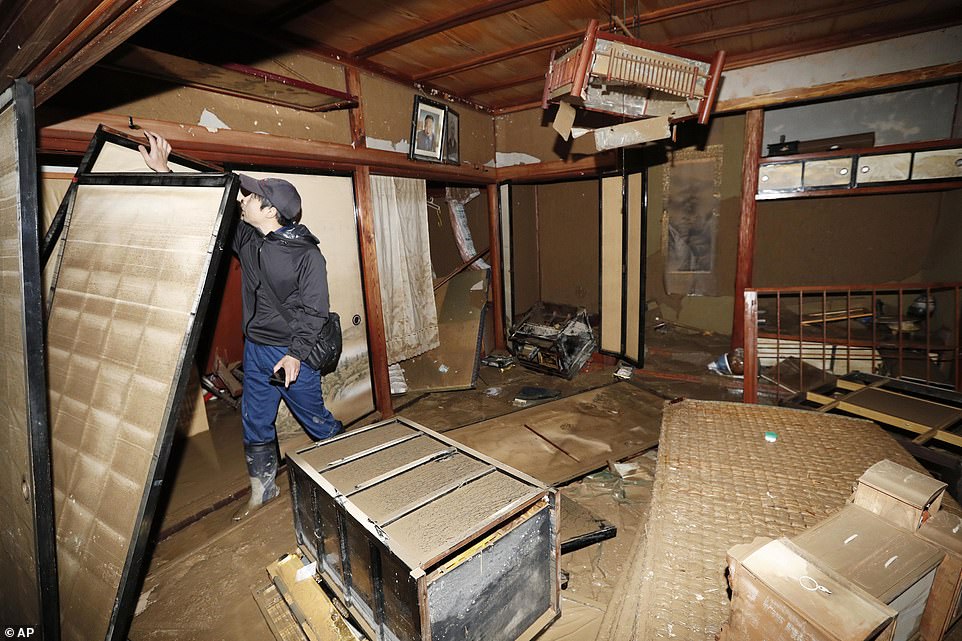 19680350-7570251-image-a-46_1571040928714 A man surveying the damage to his relative's house in Nagano, central Japan, after the devastating typhoon swept through much of the country