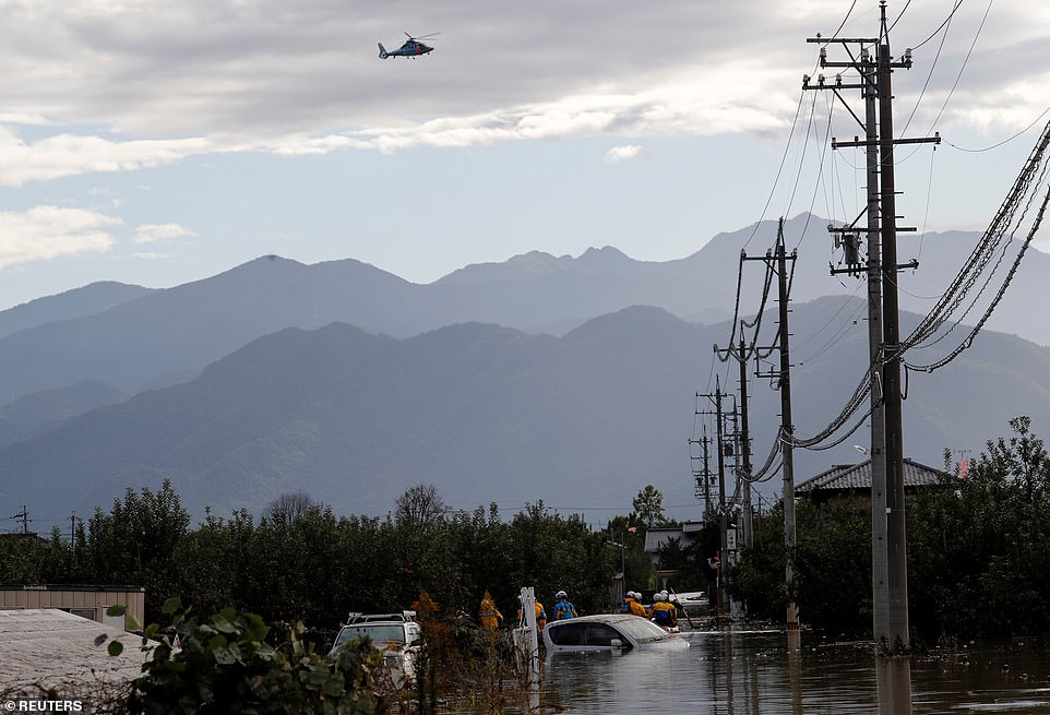 19680356-7570251-image-a-52_1571040955451 A rescue helicopter flying over rescue workers searching a flooded area in the aftermath of Typhoon Hagibis, which caused severe floods at the Chikuma River in Nagano