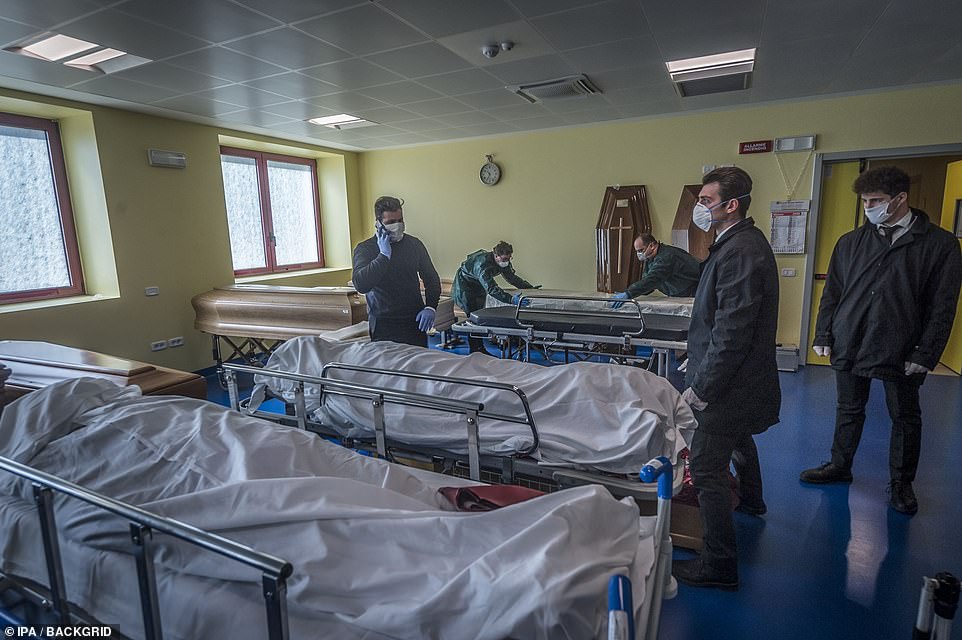 26115076-8123307-image-a-21_1584531993499 Hospital workers in face masks stand over trolleys at the Ponte San Pietro hospital in Bergamo on Tuesday as they prepare coffins
