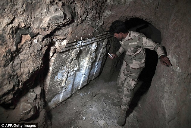 Archaeologists assessing the damage caused by Islamic State militants to the tomb of the prophet of Jonah have found an undiscovered palace. Here, a member of the Iraqi army stands next to  Assyrian stone sculptures of demi-goddesses, pictured spreading the 'water of life'