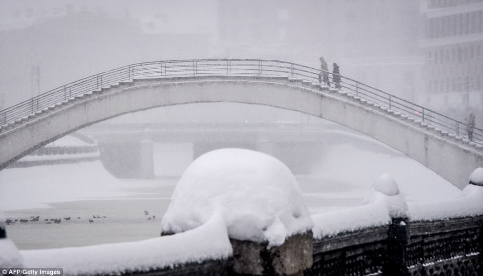 People were pictured crossing a bridge in Moscow as extreme weather that looks set to worsen brought snow, sleet and power shortages to the capital and surrounding region 