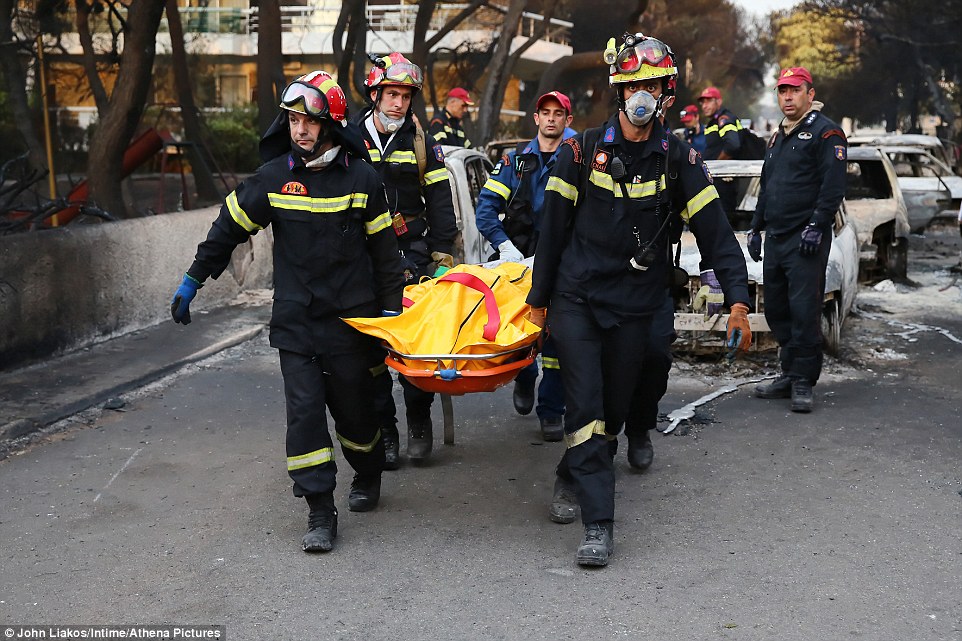 Fire fighters carry the body of a victim through the streets of Mati this morning as emergency crews sifted through the remains of burnt out cars