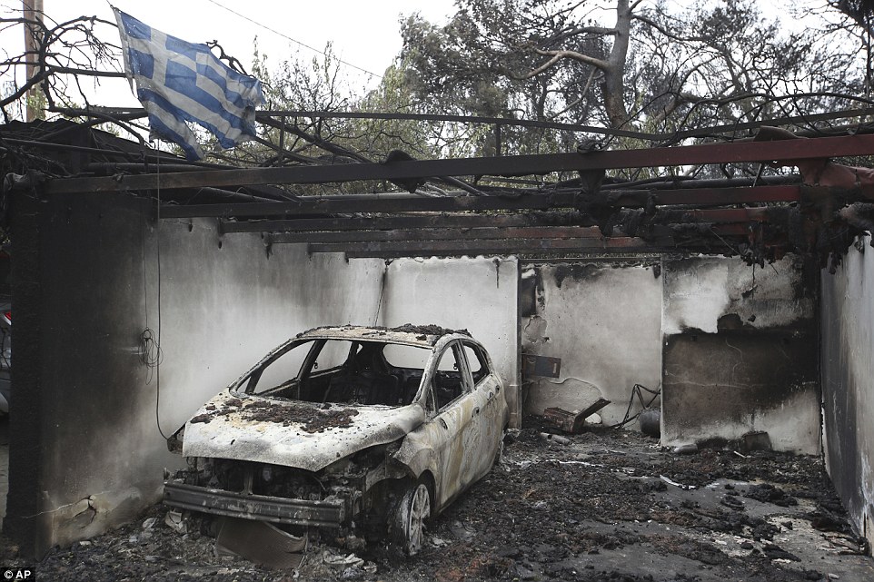 The ragged remains of a Greek flag are seen above a burnt out car in a garage of a house ruined by fire in Mati this morning