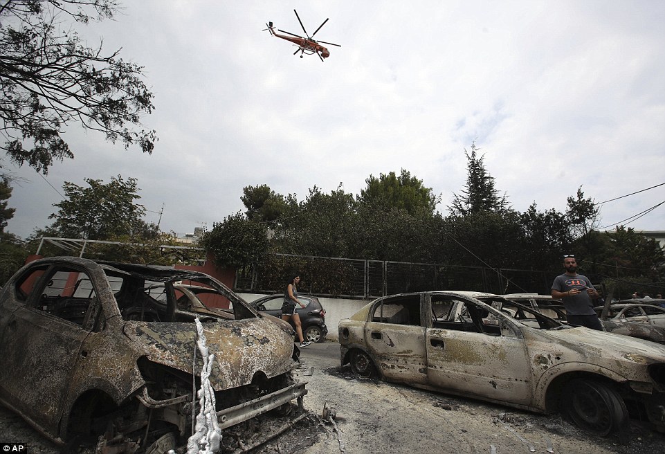 Emergency response: A water-carrying helicopter flies overhead as people survey the damage from devastating wildfires in Mati