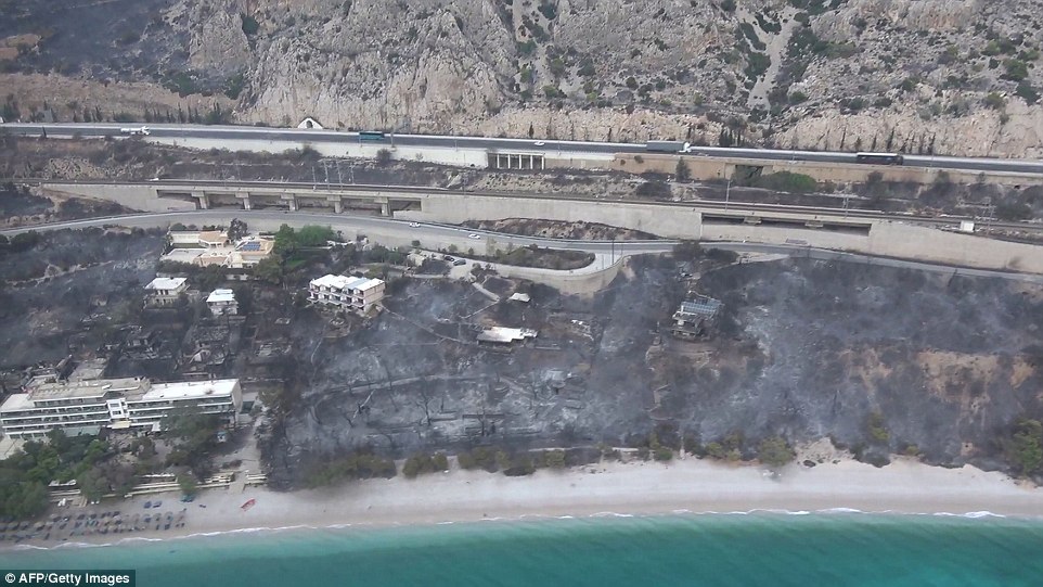 Another aerial photograph shows how flames came right down to the coastline in Kineta, tearing through woodland and leaving buildings in ruins
