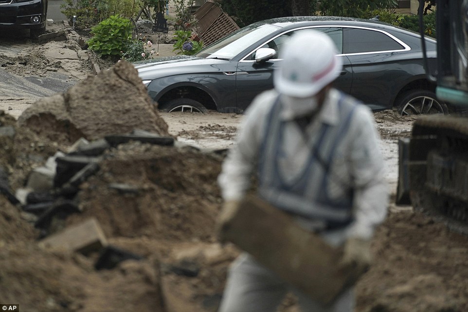4fdcae3100000578-6145357-image-a-20_1536395960560 A worker removes heavy debris from a damaged street as a vehicle half buried in mud can be seen behind him in the street