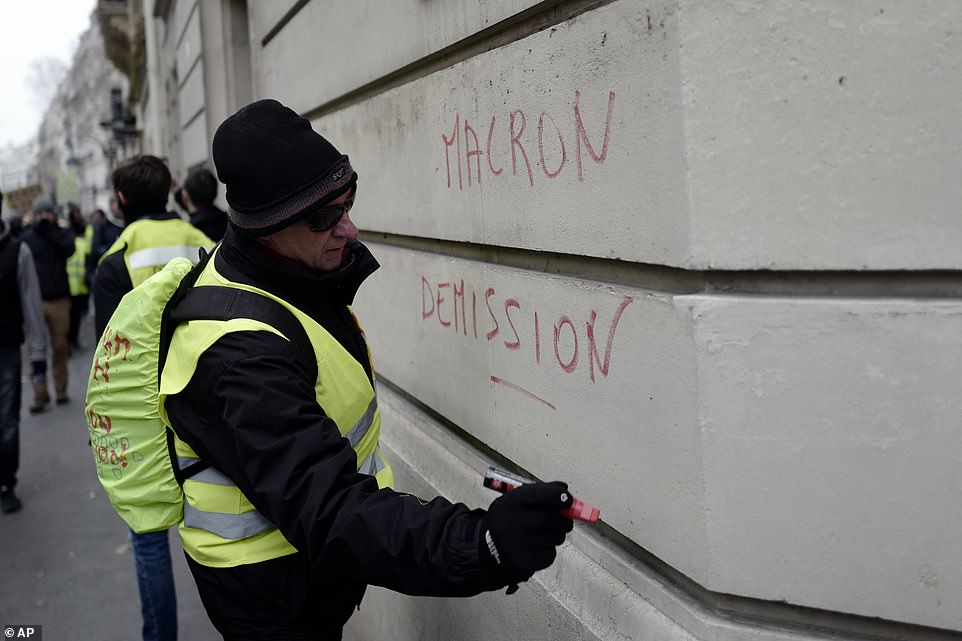 7457932-6498733-image-a-38_1544870589676 A demonstrator wearing a yellow vest vandalises 'Macron resign' on a wall during Saturday morning protests