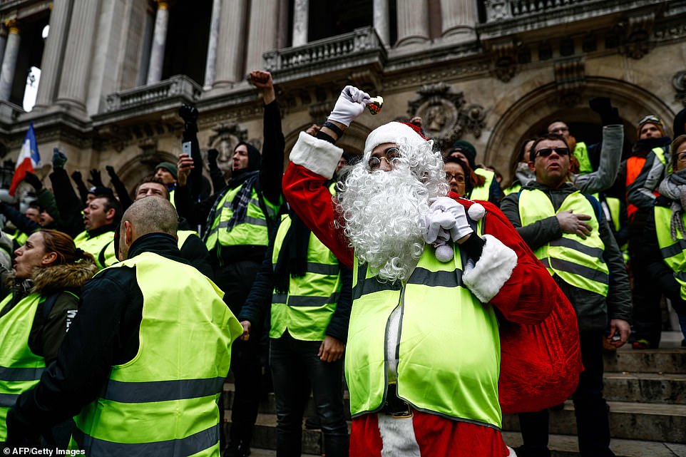 7457936-6498733-image-a-33_1544870419555 A protester dressed as Santa Claus, holding a sack of presents, stands on the steps of the Opera Garnier in Paris and chants for President Emmanuel Macron to resign