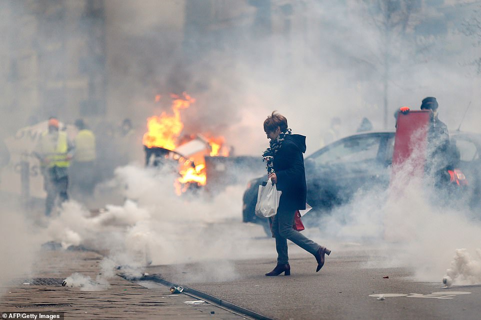 8158522-6560213-image-a-46_1546694686925 A woman walks through smoke passing burning material during a rally by yellow Vest anti-government protesters in Rouen. This is the eighth Saturday of protests called by the grass-roots movement