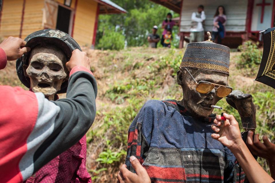 A local puts a sunhat on one corpse, while the other gets a pair of sunglasses and a cigarette before they're taken for a stroll