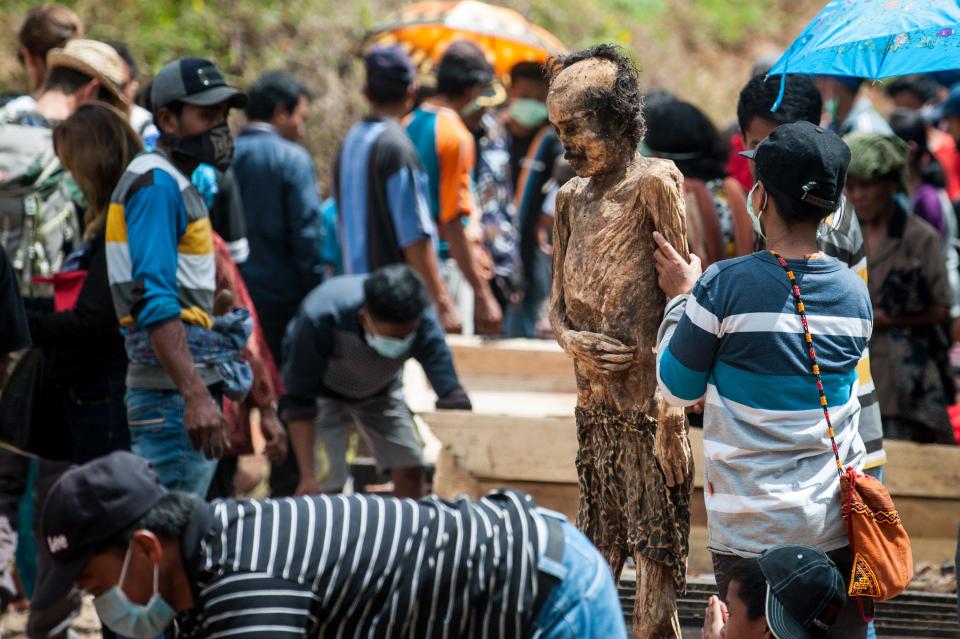 The locals help each other to undress what appears to be a woman's corpse