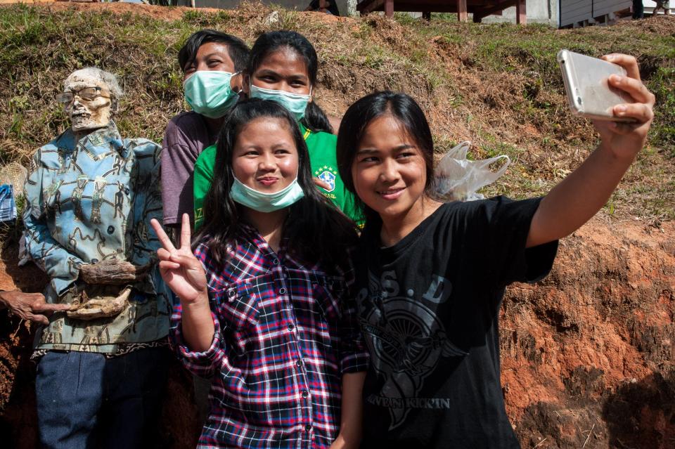 Young girls pose for a selfie in front of their relative's corpse