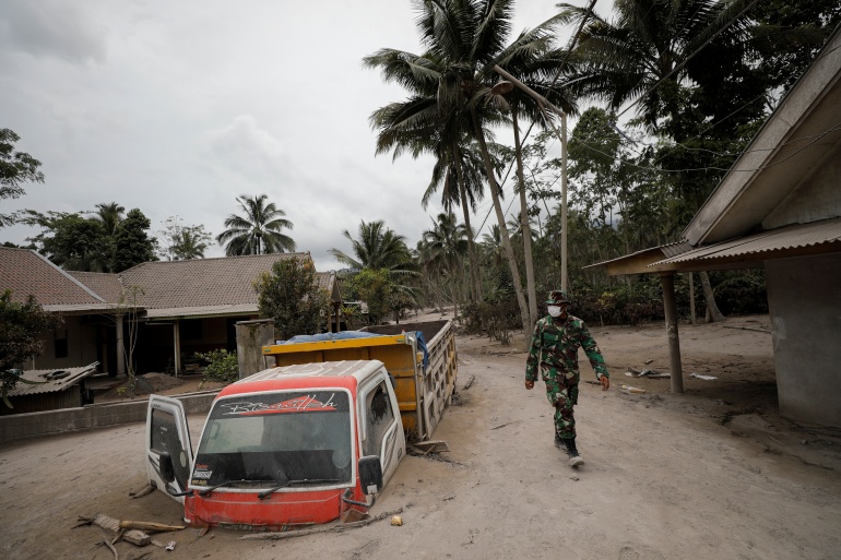 An Indonesian soldier walks past damage trucks at Sumberwuluh village following the eruption of Semeru mount volcano in Lumajang regency