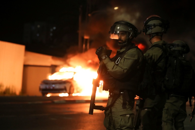 rtxc8nn9 Israeli security force members stand near a burning Israeli police car during clashes between Israeli police and members of the country's Arab minority in the Arab-Jewish town of Lod