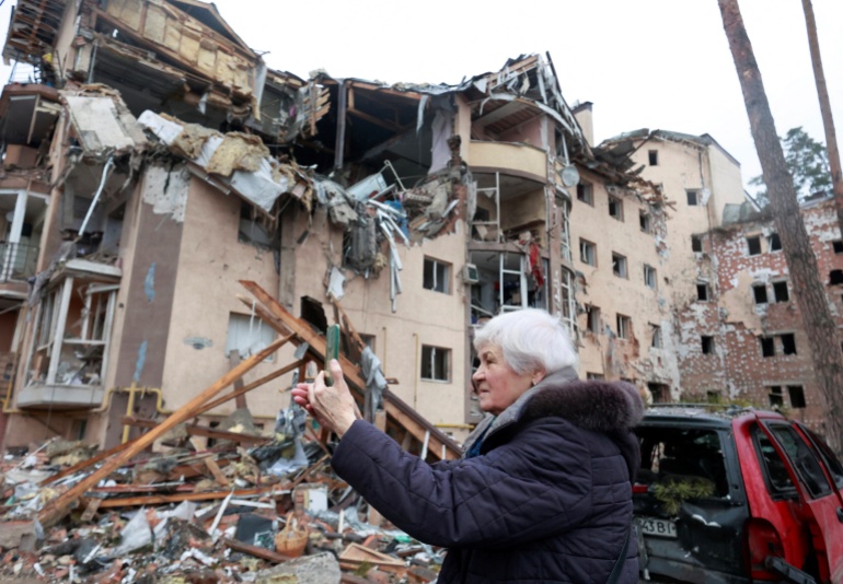 rts5y6nt A woman uses a smartphone in front of a residential building destroyed by recent shelling in Irpin