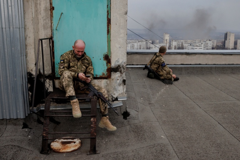 Ukrainian soldiers sit on a roof as a northern residential district in Kharkiv is shelled from Russian positions in as Russia's attack on Ukraine continues