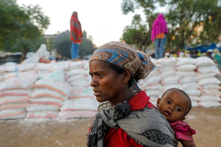 rtxd4r62 Woman carries an infant as she queues in line for food, at the Tsehaye primary school, in Shire